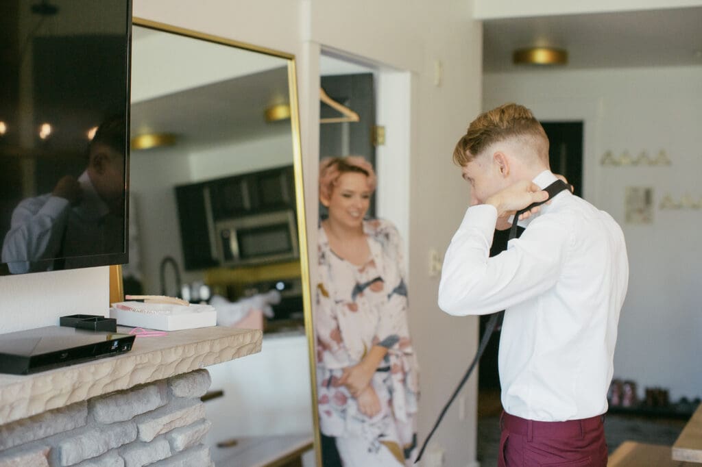 A bride watches her groom get ready in his wedding clothes in Mammoth Lakes, California.