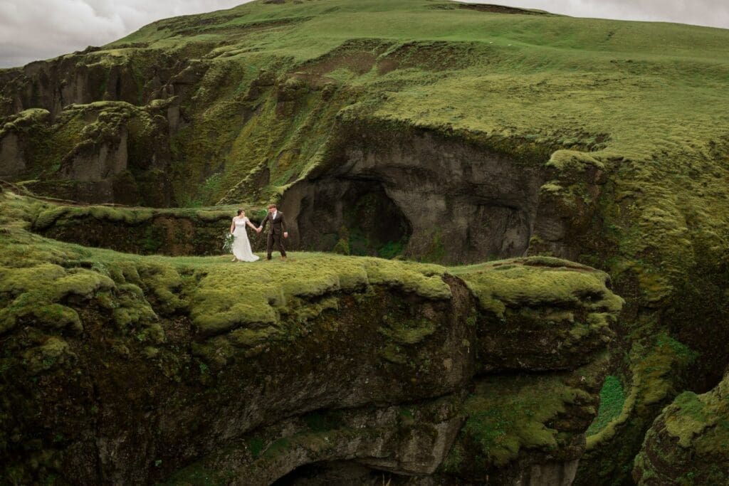 A bride and groom walk on a grassy hillside in Iceland.