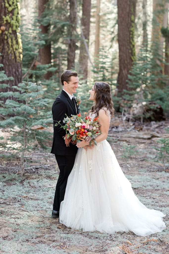 A bride and groom look at each while dressed in their wedding clothes in Yosemite