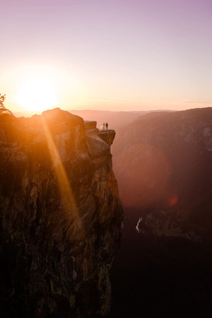 A bride and groom stand on the towering cliff at Taft Point in Yosemite.