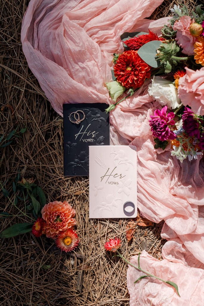 A pair of vow books for a bride and groom lay on pine needles in sunlight in Yosemite.