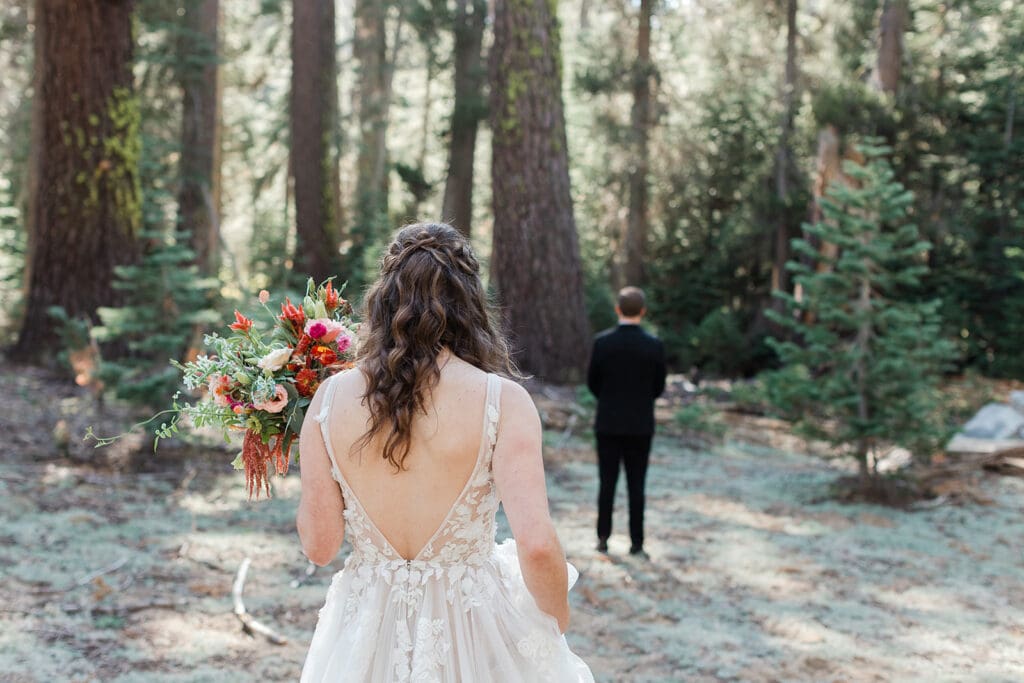 A bride approaches her groom from behind for their "first look" in Yosemite National Park