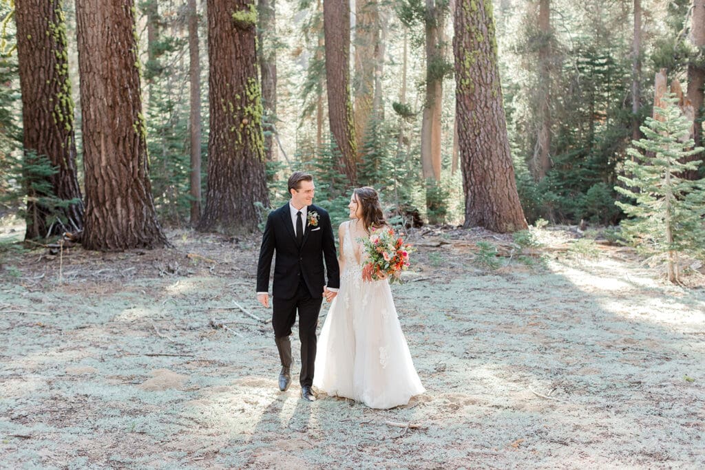 A bride and groom walk together in a wooded forest in Yosemite National Park