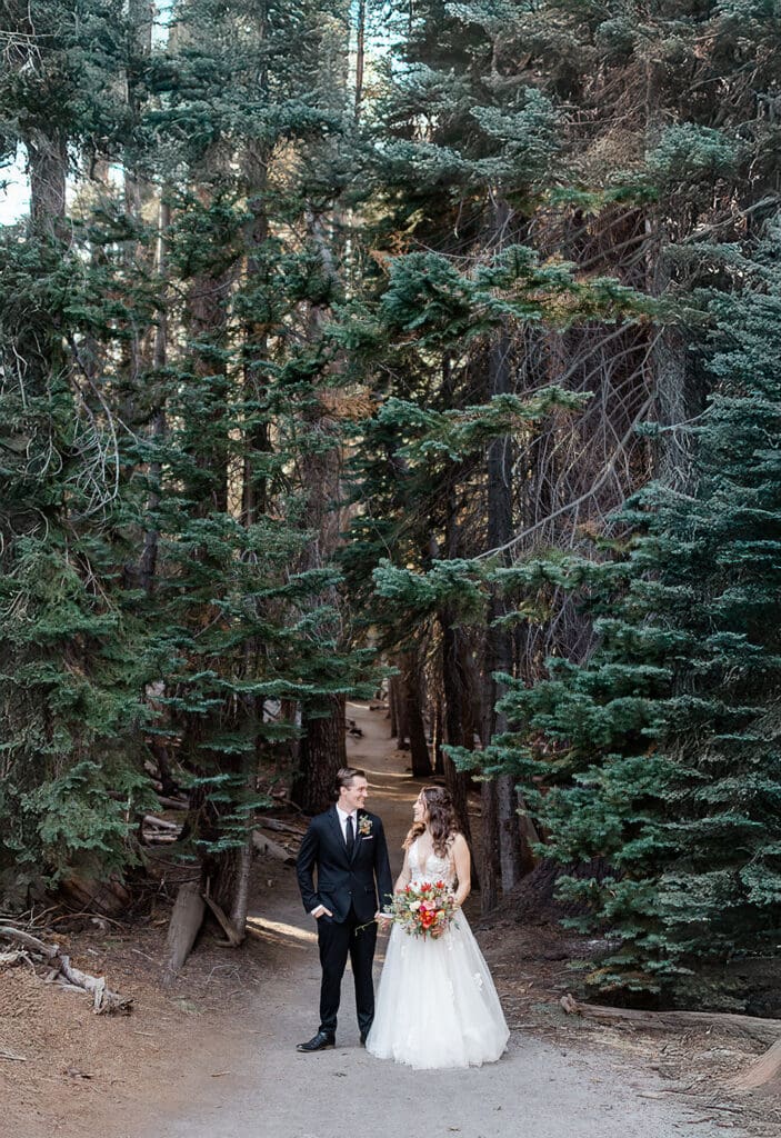 A bride and groom pose in front of trees in Yosemite National Park