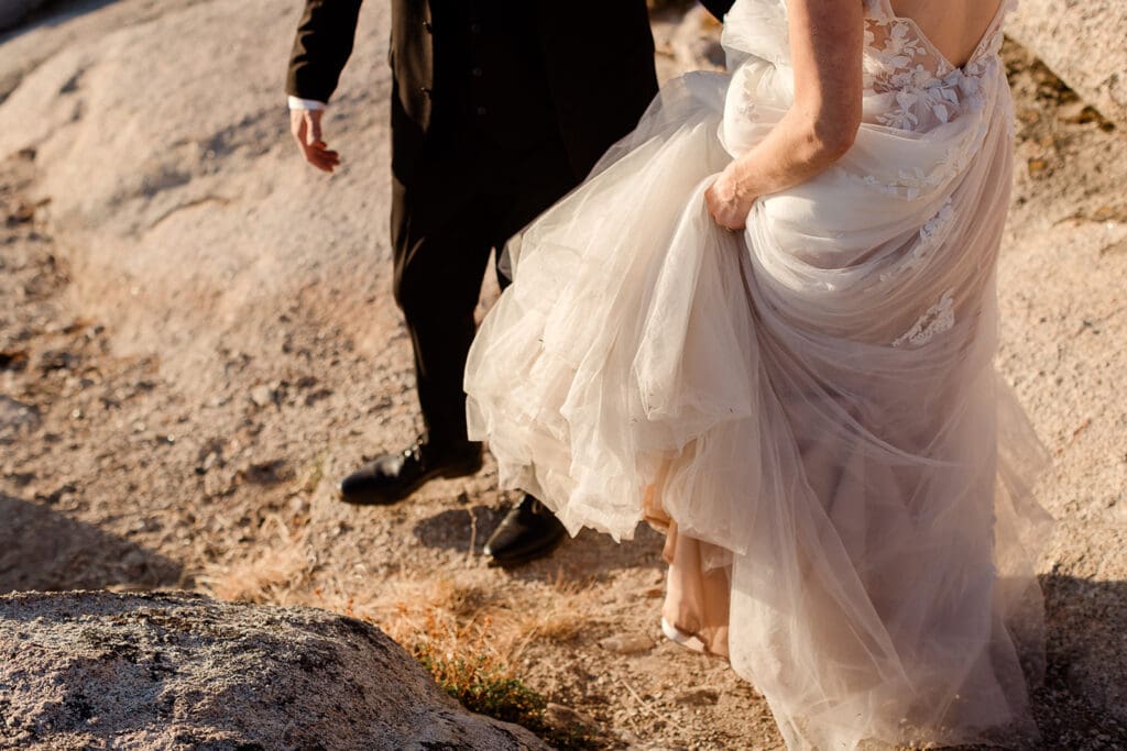 A bride scoops holds the layers of her dress as she walks around the rocks at taft poin, yosemite. 