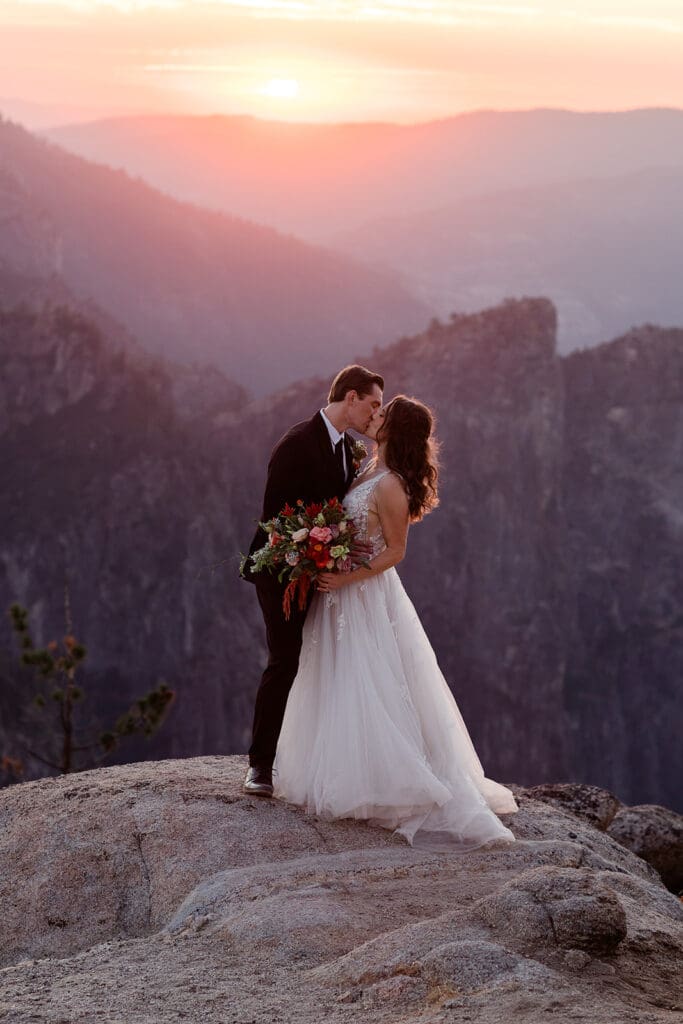 A groom kisses his bride at sunset on a cliff at Yosemite National Park.