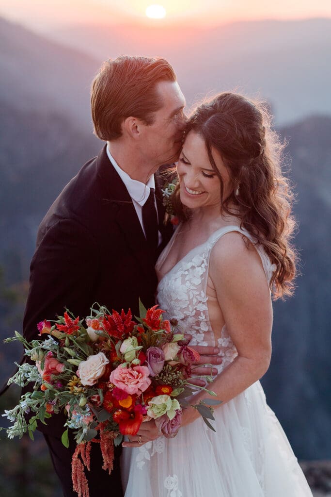 A groom kisses his bride at sunset on a cliff at Yosemite National Park.