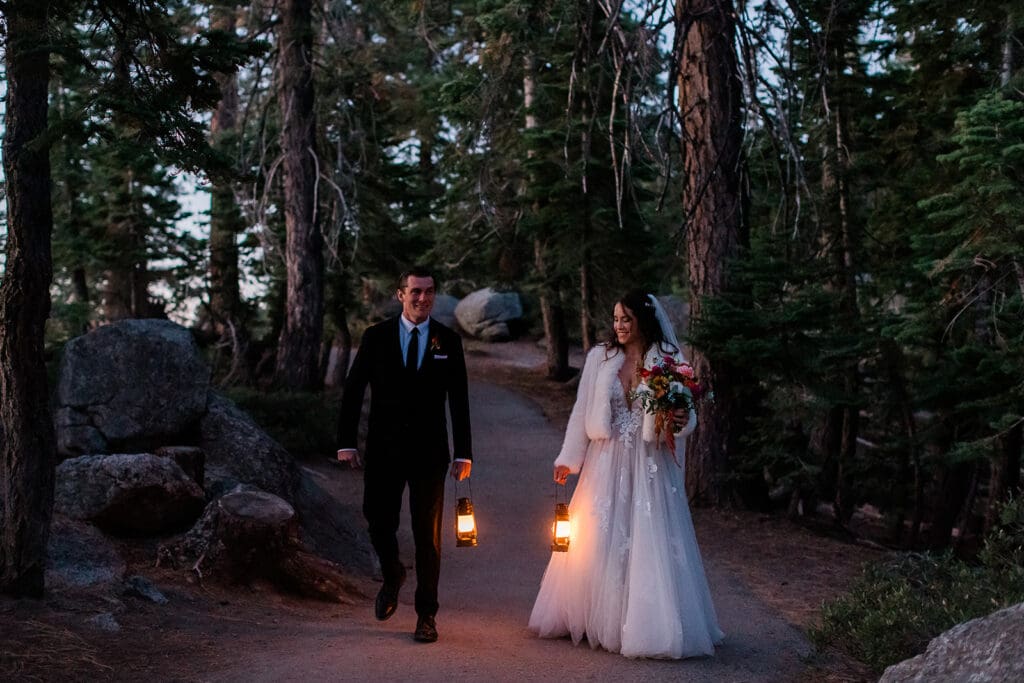 A bride and groom walk in the dark of twilight carrying lanterns in Yosemite.