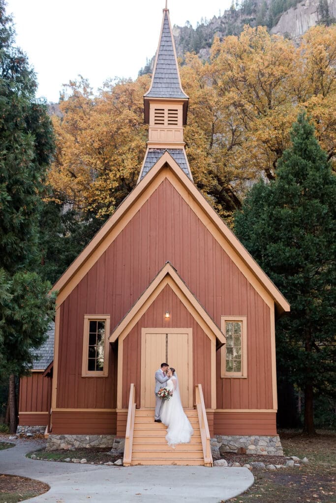 A bride and groom kiss on the steps of the Yosemite Wedding Chapel