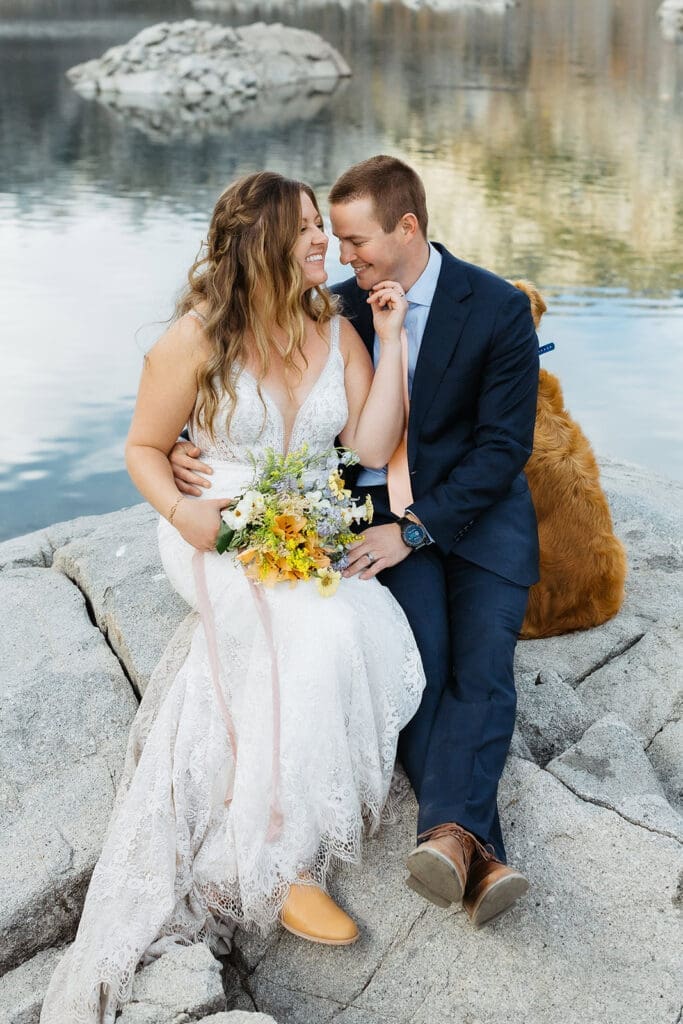 A bride and groom sit on a rock with their dog by a lake in Inyo National Forest.
