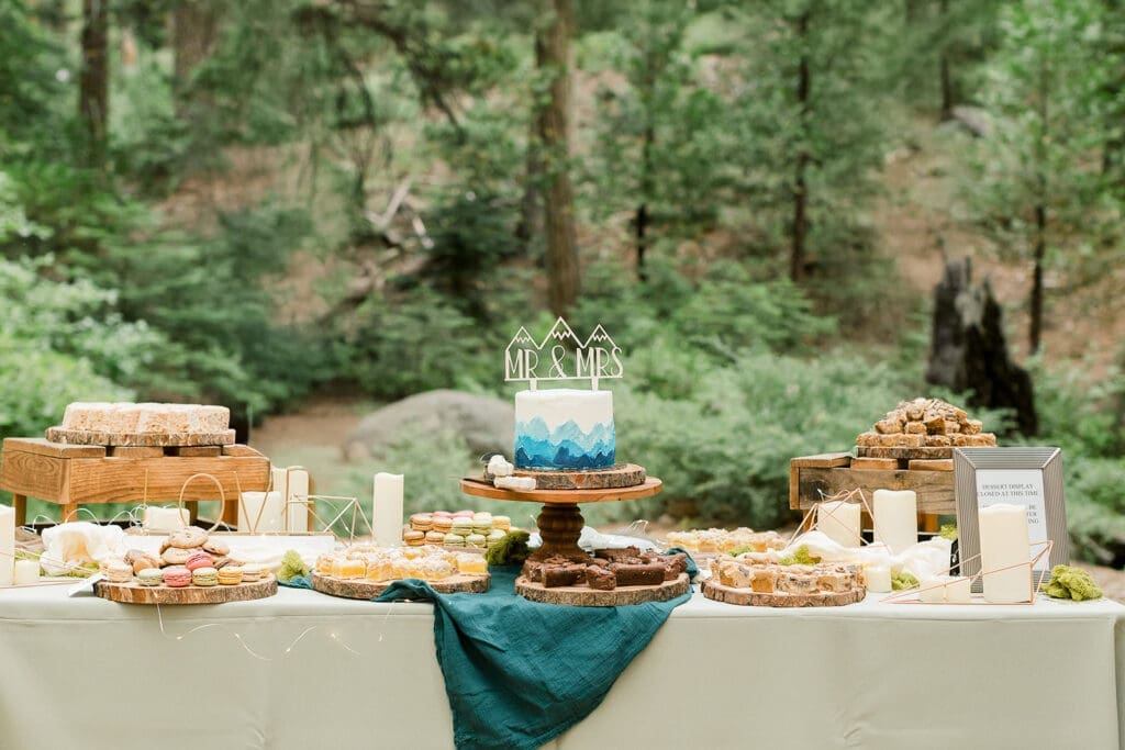 A wedding cake on a dessert table in a forest setting