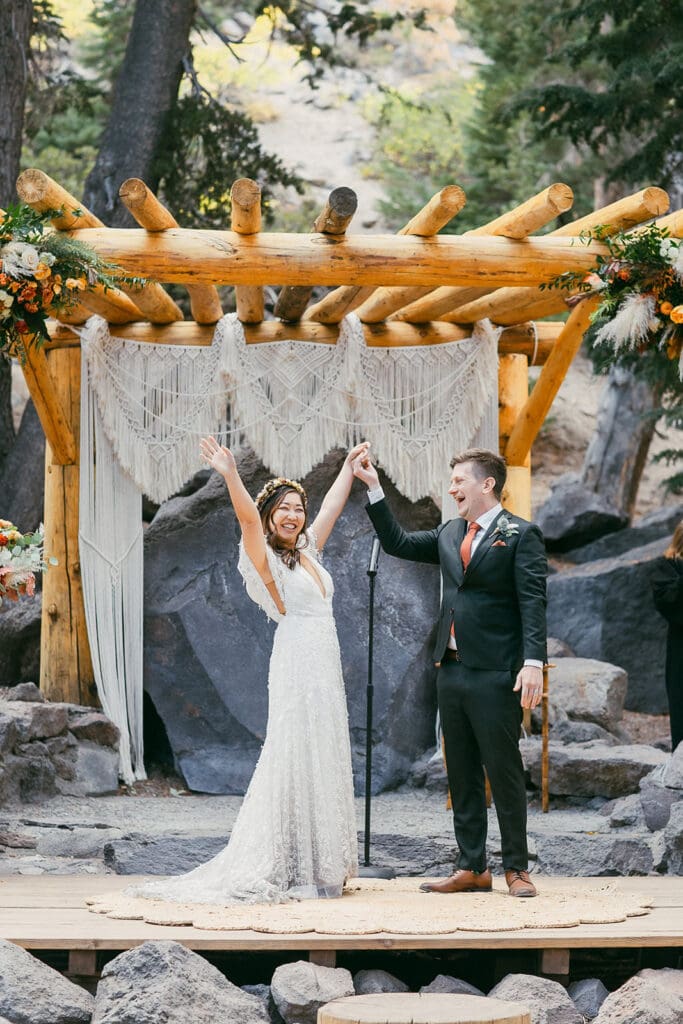 A bride and groom raise their hands in celebration shortly after saying their vows at the Forest Chapel at Twin Lakes in Mammoth.