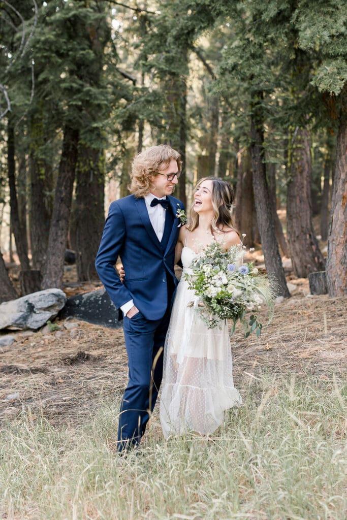 A bride and groom laugh in a forest on their wedding day in Mammoth Lakes.