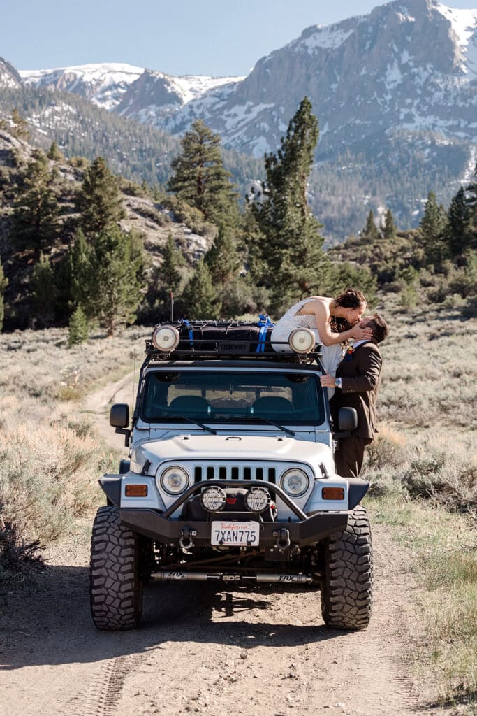 A bride sits on top of a jeep while leaning down to kiss her groom on their wedding day in mammoth Lakes.