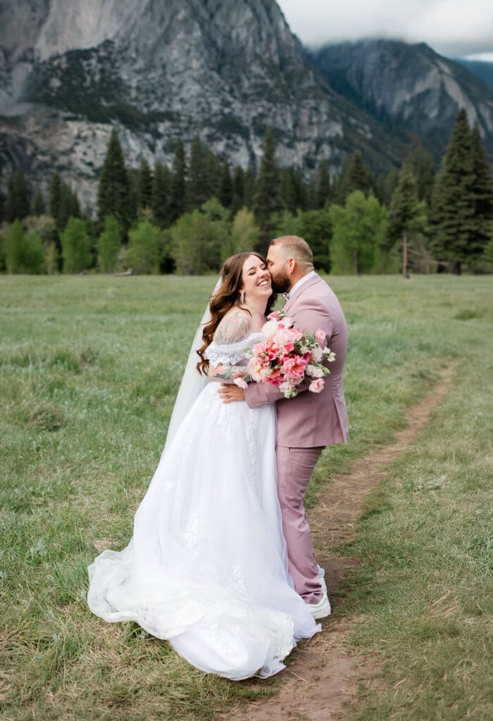 A groom kisses his bride in a yosemite meadow